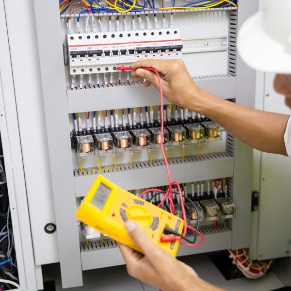 Electrician engineer work tester measuring voltage and current of power electric line in electical cabinet control.